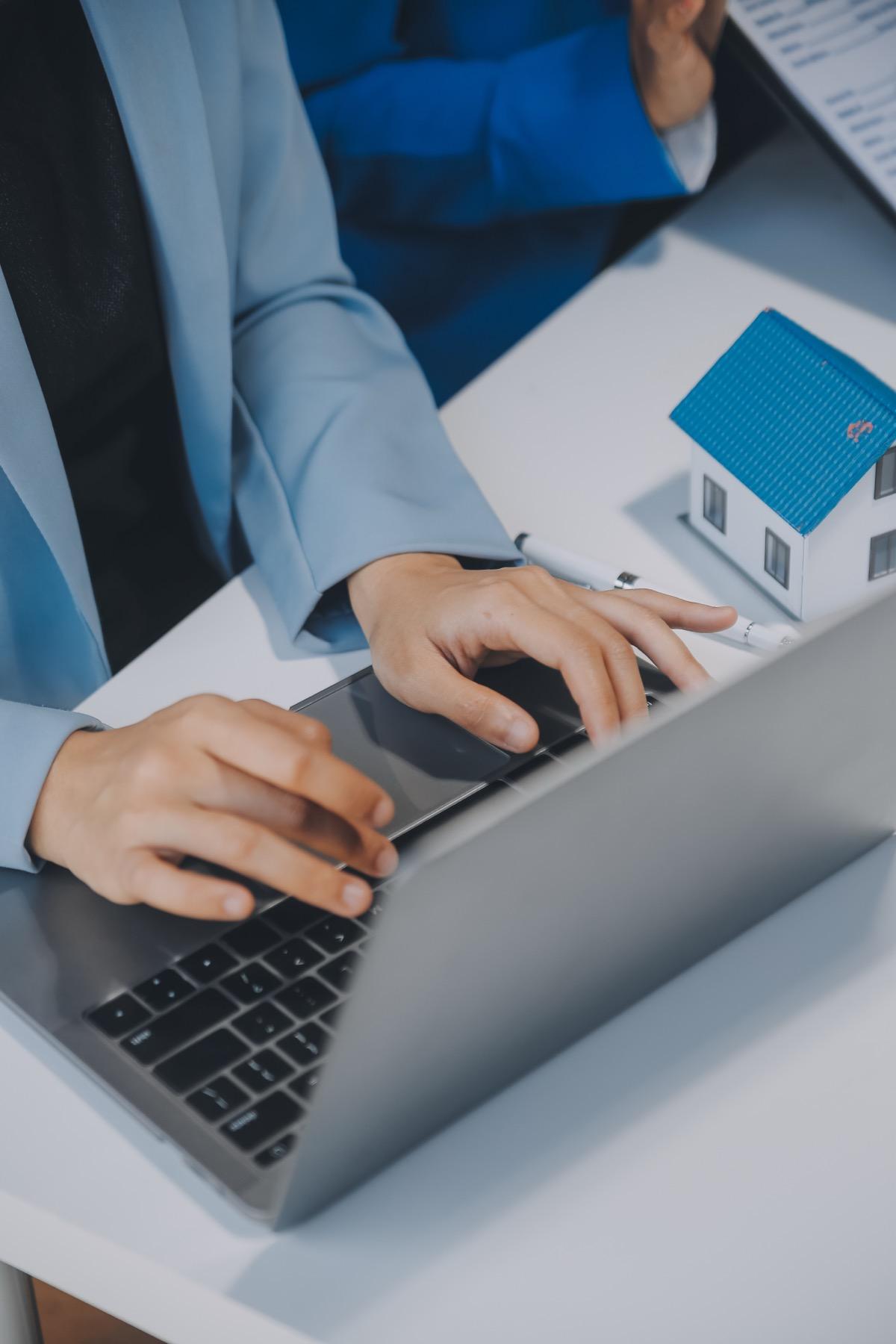 Corretor utilizando notebook ao lado de maquete de imóvel